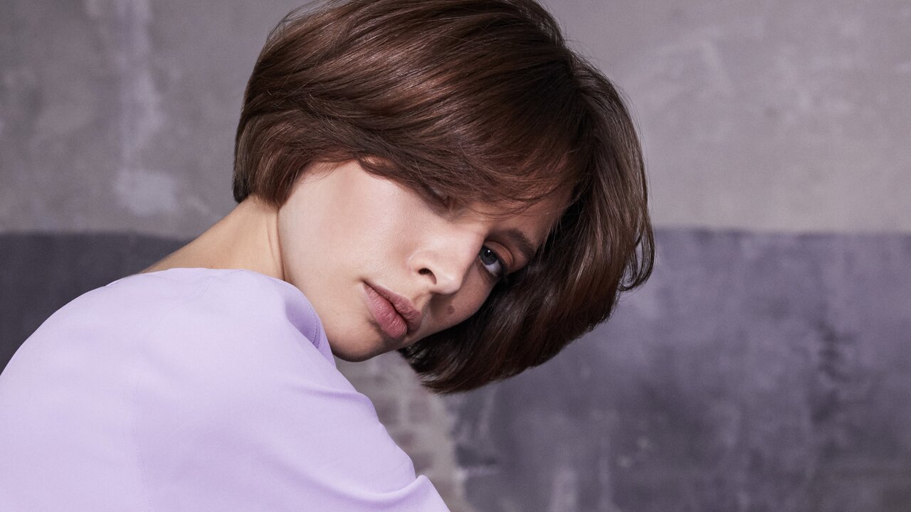 5 Haarpflege-Tipps helfen die Haarfarbe lange strahlen zu lassen Portrait einer schönen brünetten Frau mit Bob-Frisur und fliederfarbenem Kleid