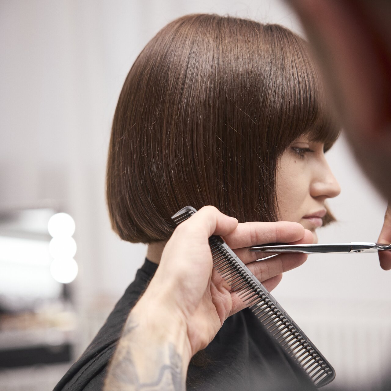 Einer jungen Frau mit mittellangem Haar wird ein kinnlanger Bob geschnitten