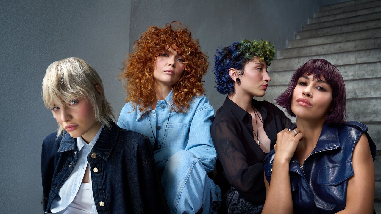 Vier Models mit unterschiedlichen, farbintensiven Frisuren posieren modern inszeniert vor einer Treppe.