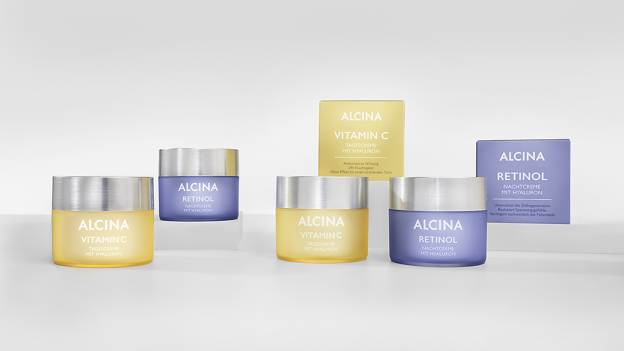 Je zwei Tiegel ALCINA Vitamin C Creme mit gelber Verpackung und Tiegel ALCINA Retinol Creme mit violetter Verpackung auf durchsichtigem Sockel platziert