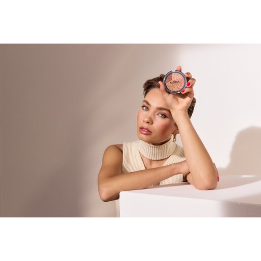 Junge schöne Frau mit geschminktem Gesicht stützt sich mit dem Arm auf einer Box ab und hält den ALCINA Powderblush in einer Hand, der für den Make-up-Trend Douyin Blush verwendet werden kann, da er vier verschiedene Farbnuancen enthält