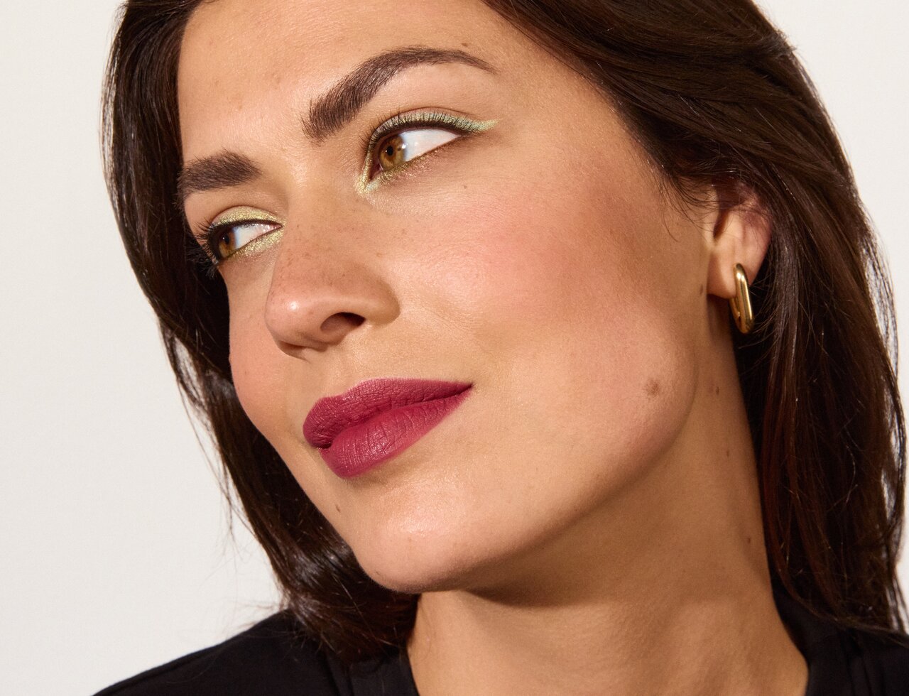 Schöne junge Frau mit braunen Haaren im Profil, der Fokus liegt auf den kräftig geschminkten Lippen in Beerenton, die den Make-up-Trend Matte Cherry Lips repräsentieren