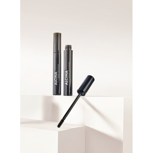ALCINA Wonder Volume Mascara in glänzender dunkelgrauer Hülse mit geöffnetem Bürstchen, auf weißen Podesten platziert. Für intensiv voluminöse Wimpern.