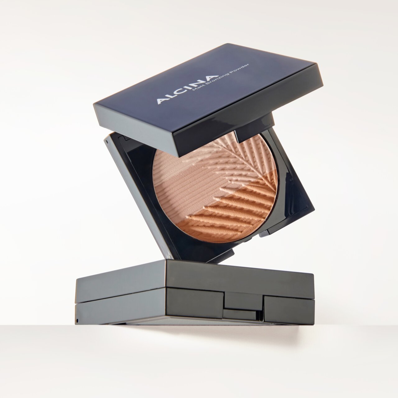 ALCINA Matt Bronzing Powder in eleganter dunkler Kompaktbox mit aufgeklapptem Deckel, das gepresste Puder in warmem Bronzeton mit feiner Reliefstruktur präsentiert.