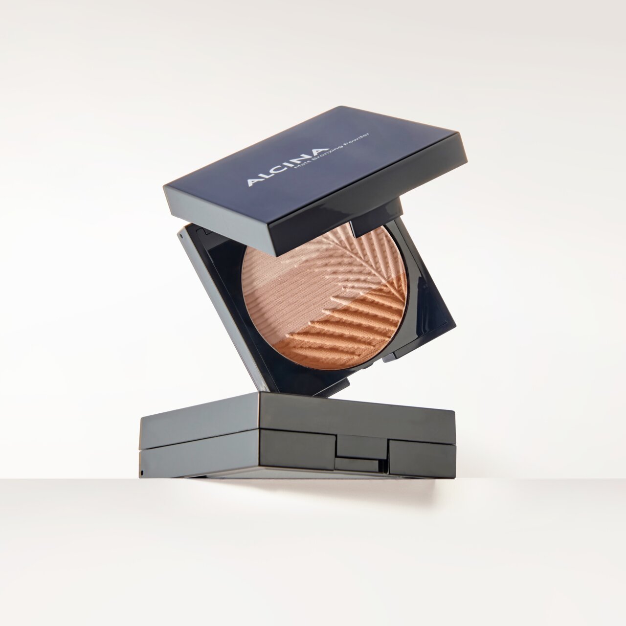 ALCINA Matt Bronzing Powder in eleganter dunkler Kompaktbox mit aufgeklapptem Deckel, das gepresste Puder in warmem Bronzeton mit feiner Reliefstruktur präsentiert.