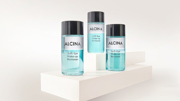 ALCINA Soft Eye Make-up Remover in drei transparenten Flaschen mit zweiphasiger, türkisfarbener Formulierung, auf weißen Podesten arrangiert für sanftes und gründliches Entfernen von Augen-Make-up.