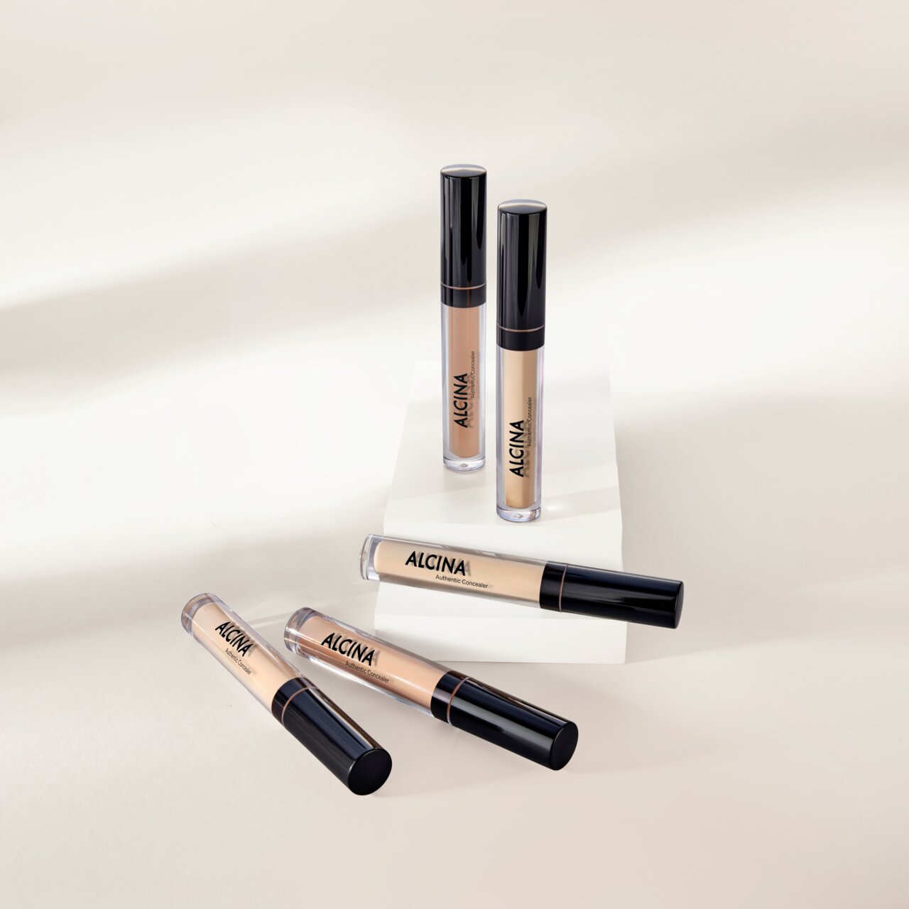 Mehrere ALCINA Authentic Concealer in verschiedenen Nuancen liegen und stehen dekorativ auf hellen Podesten.