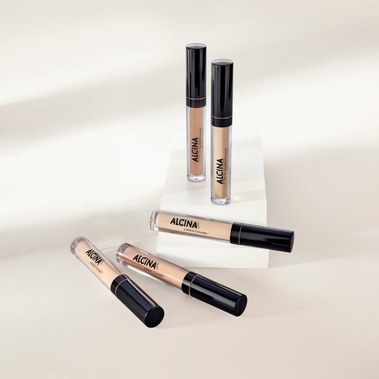 Mehrere ALCINA Authentic Concealer in verschiedenen Nuancen liegen und stehen dekorativ auf hellen Podesten.