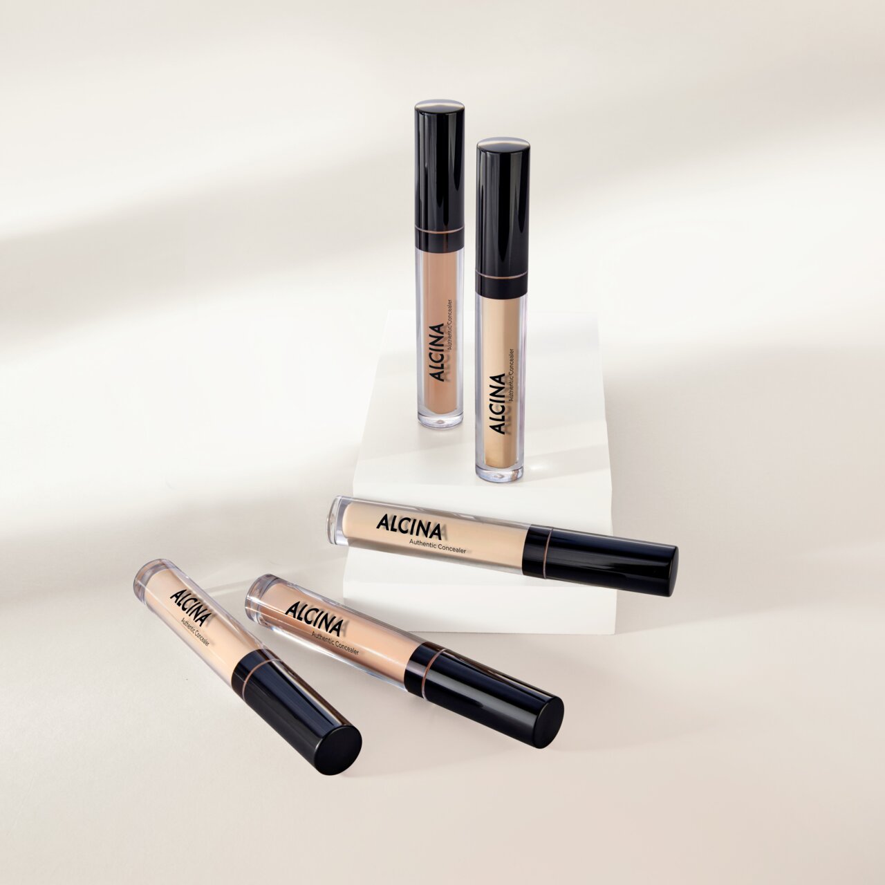 Mehrere ALCINA Authentic Concealer in verschiedenen Nuancen liegen und stehen dekorativ auf hellen Podesten.