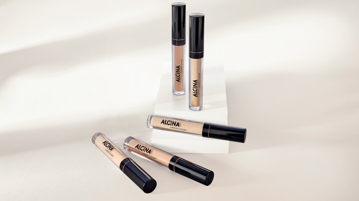 Mehrere ALCINA Authentic Concealer in verschiedenen Nuancen liegen und stehen dekorativ auf hellen Podesten.
