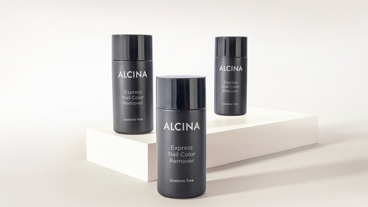 Drei schwarze Flaschen ALCINA Express Nail Color Remover stehen dekorativ auf hellen Podesten vor neutralem Hintergrund.