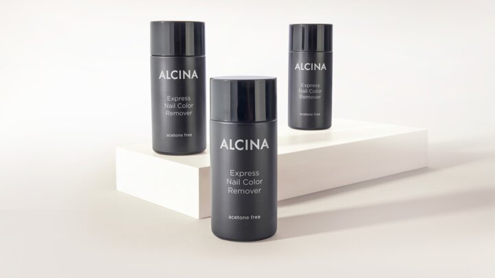 Drei schwarze Flaschen ALCINA Express Nail Color Remover stehen dekorativ auf hellen Podesten vor neutralem Hintergrund.