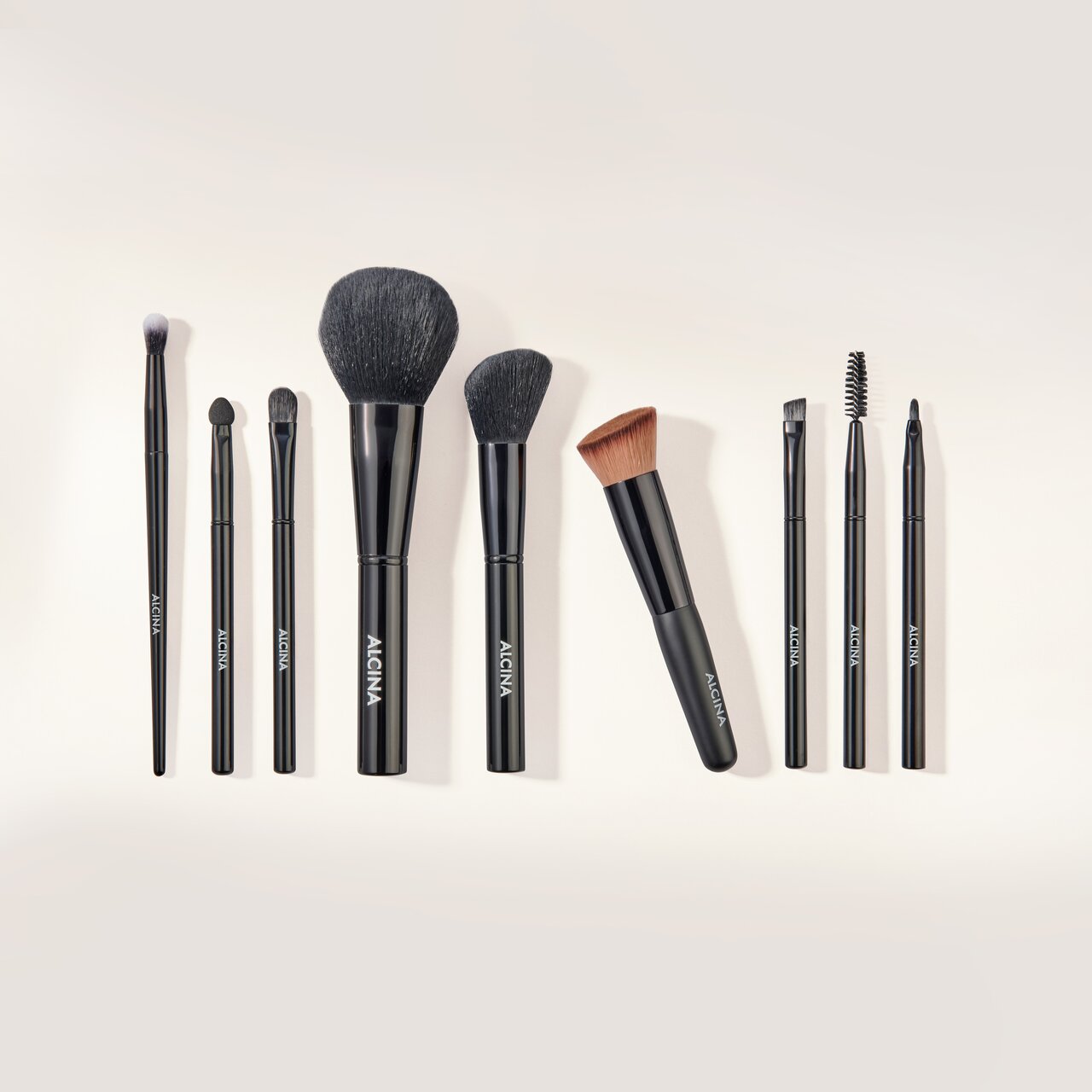 ALCINA Make-up-Zubehör mit verschiedenen Pinseln und Wimpernbürste ordentlich nebeneinander angeordnet.