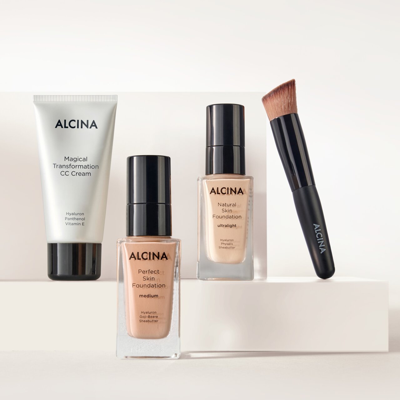 ALCINA Teint-Produkte bestehend aus Magical Transformation CC Cream, Perfect Skin Foundation in verschiedenen Nuancen und Foundationpinsel dekorativ auf hellen Podesten arrangiert.