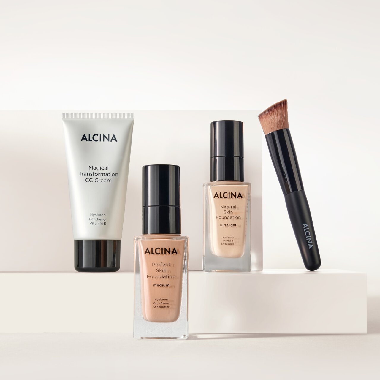 ALCINA Teint-Produkte bestehend aus Magical Transformation CC Cream, Perfect Skin Foundation in verschiedenen Nuancen und Foundationpinsel dekorativ auf hellen Podesten arrangiert.