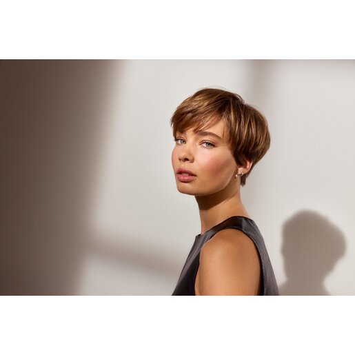 Frau mit kurzem, braunem Haar in ärmellosem, dunklem Oberteil steht seitlich im Licht, das Make-up ist dezent mit schön geschminkten Lippen.