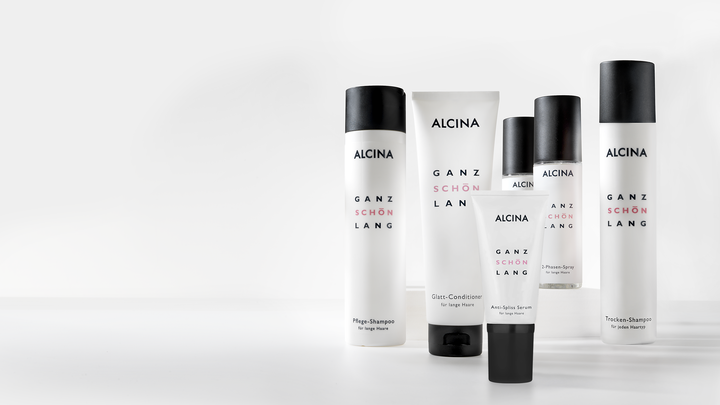 ALCINA „Ganz schön lang“-Pflegeserie für langes Haar in schlichtem weiß-schwarzen Design, mit verschiedenen Shampoos, Conditionern und Sprays, die in einer Reihe für eine übersichtliche Produktpräsentation angeordnet sind.