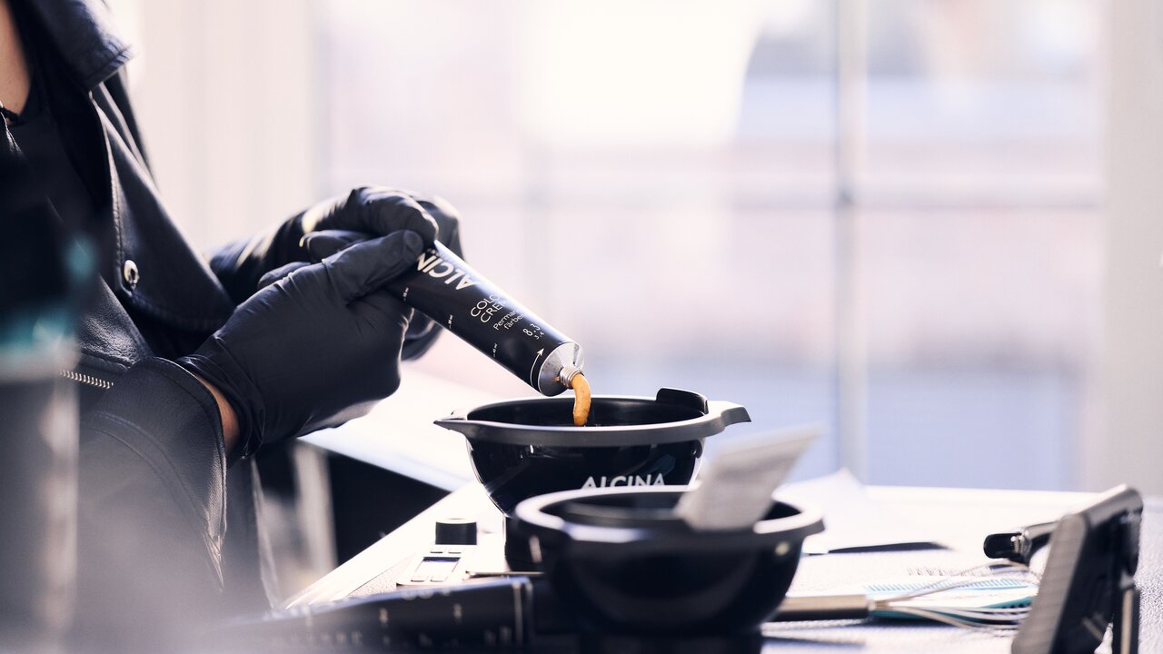 Friseurin mit schwarzen Handschuhen drückt ALCINA Color Creme in eine ALCINA Färbeschale, um eine professionelle Haarcoloration vorzubereiten.