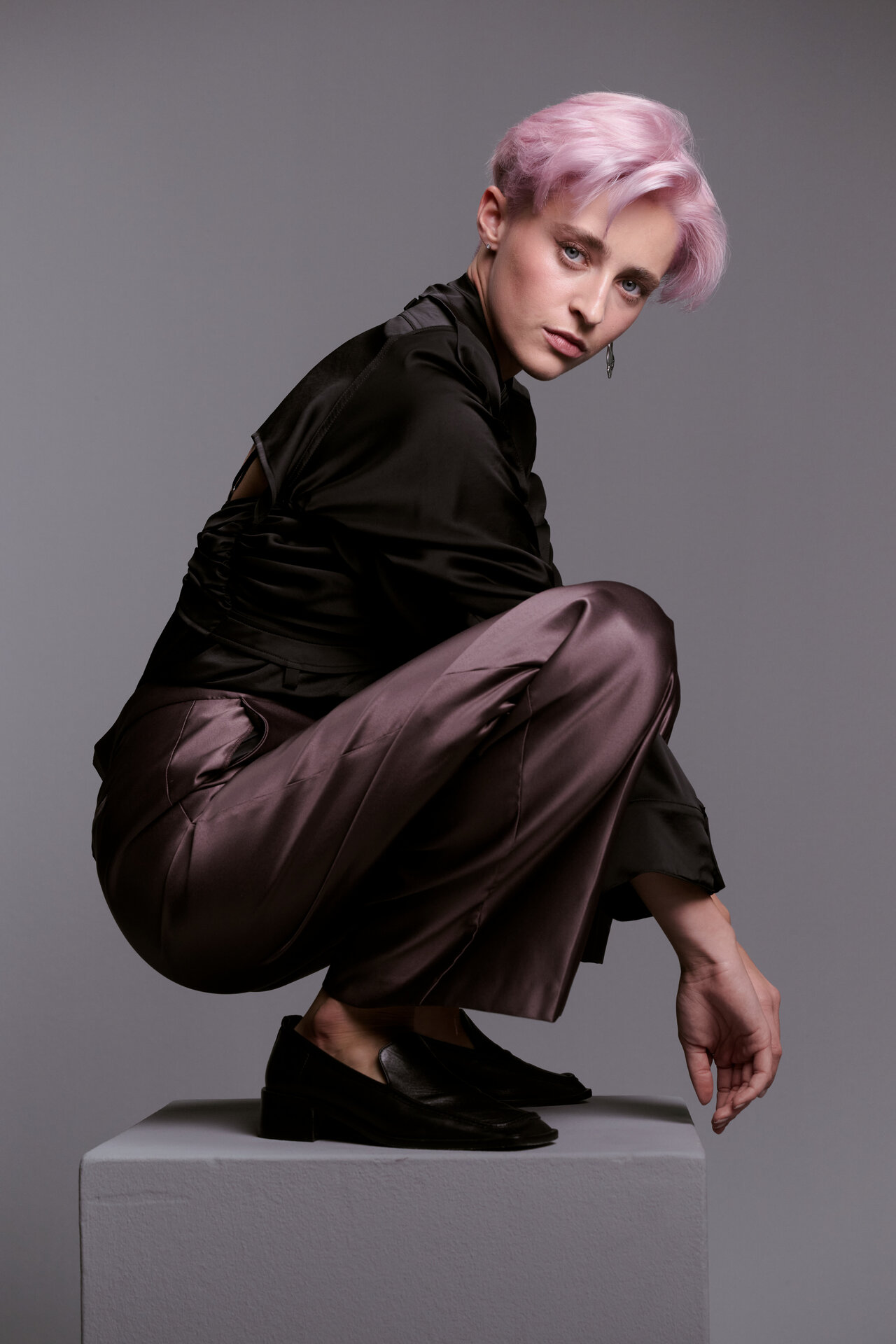Model mit kurzem, rosafarbenem Haar als Ergebnis einer ALCINA Blondveredelung posiert in dynamischer Haltung vor grauem Hintergrund.