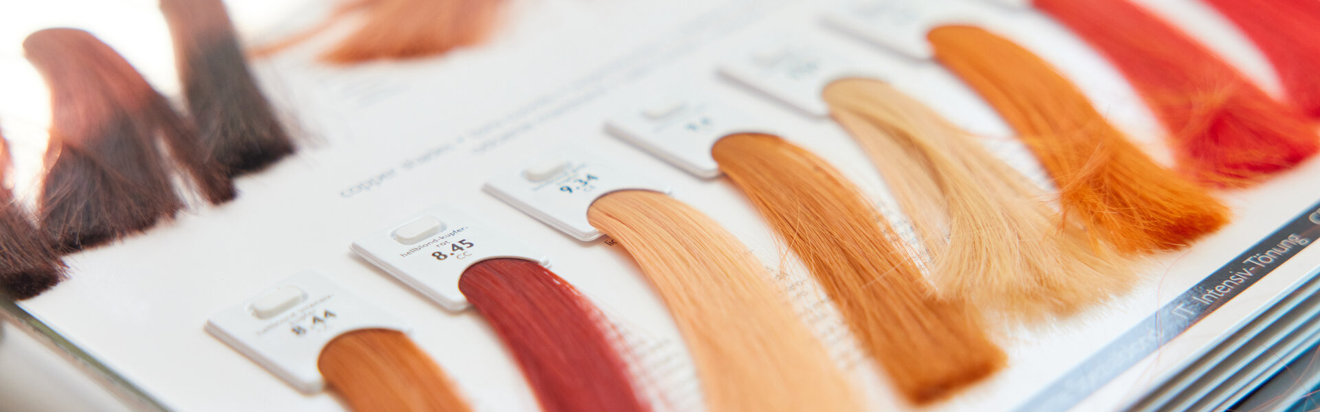 Nahaufnahme eines aufgeschlagenen Farbbuchs, wie es in Friseursalons zum Einsatz kommt. Mit gefärbten Haarsträhnen in verschiedenen Rottönen.