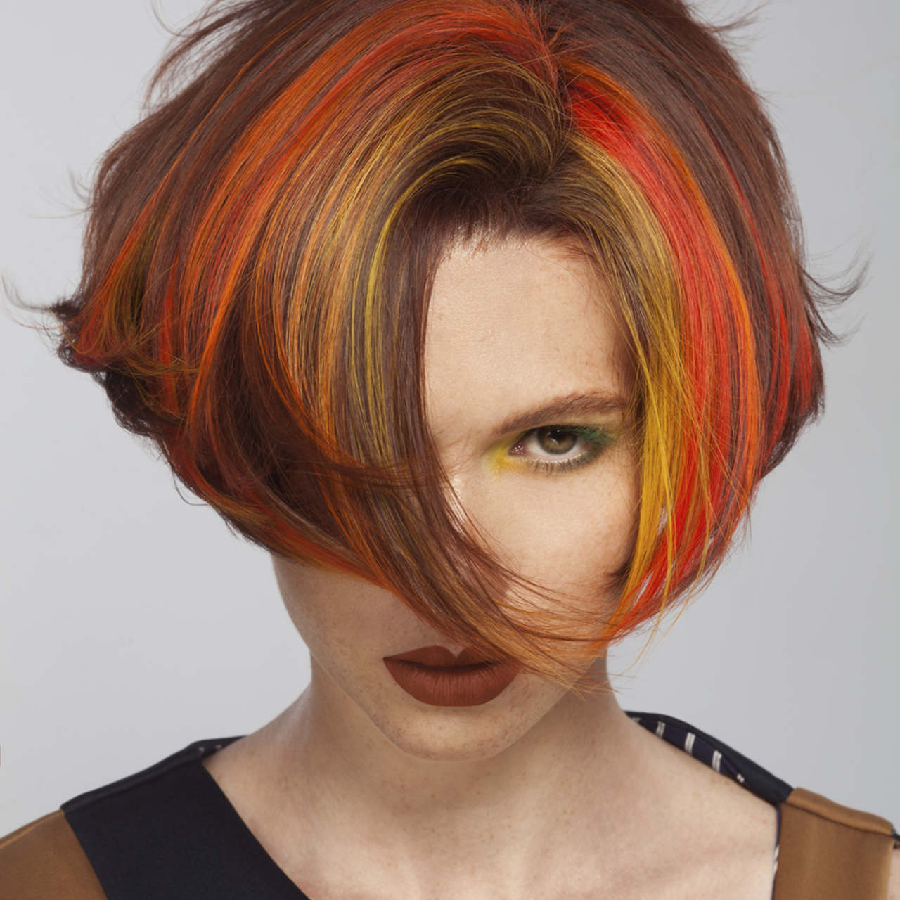 Portrait einer Frau mit kurzer Bob-Frisur und gefärbten Blocksträhnen als Chunky Highlights in Orange,  Rot und Gelb