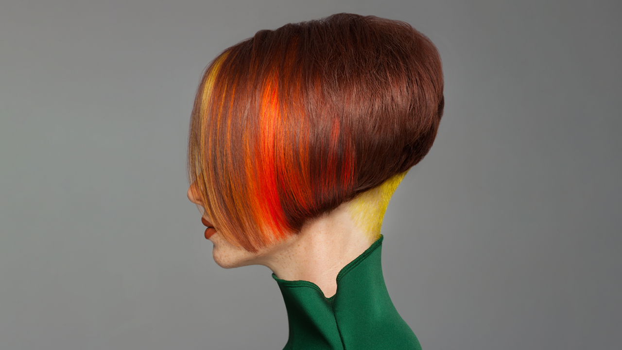 Portrait einer Frau in der Seitenansicht mit roter Bob-Frisur und im unteren Deckhaar eingefärbten Blocksträhnen in der Chunky Undercut-Technik in Orange, Rot und Gelb