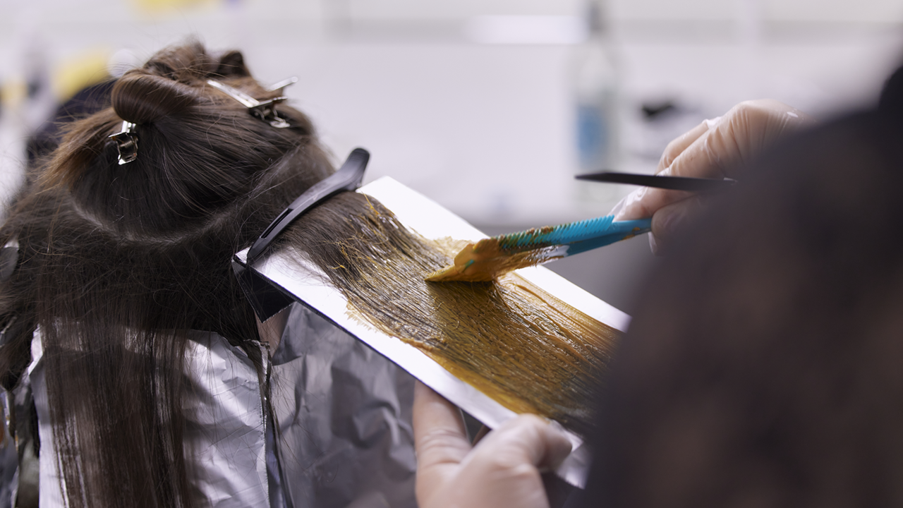 Wie auch bei Balayage sollten Haare im Ombré-Stil mit professionellen Haarfarben beim Friseur gefärbt werden Rückansicht einer Frau, bei der gerade die Ombre und Balayage Haarfärbetechnik mittels Pinsel-Farbauftrag und Folientechnik durchgeführt wird