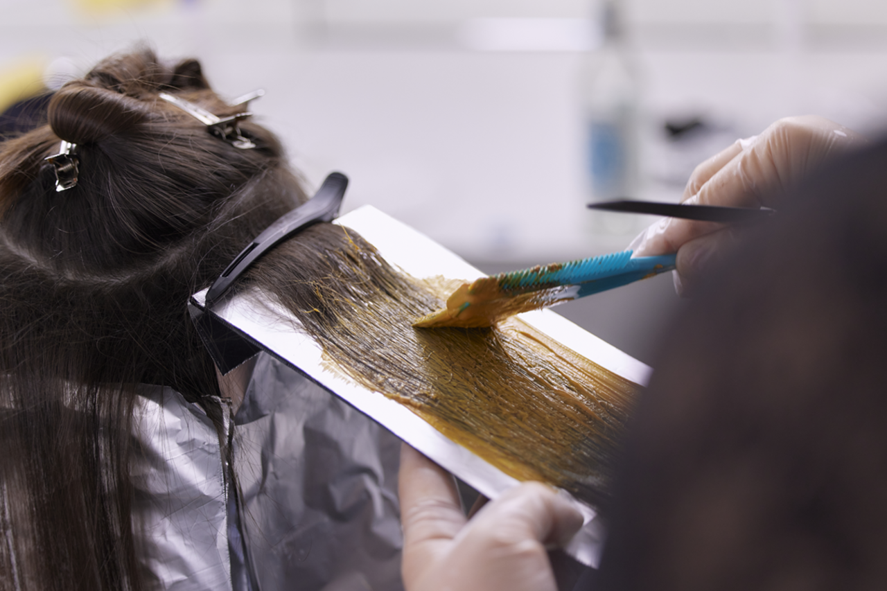 Rückansicht einer Frau, bei der gerade die Ombre und Balayage Haarfärbetechnik mittels Pinsel-Farbauftrag und Folientechnik durchgeführt wird