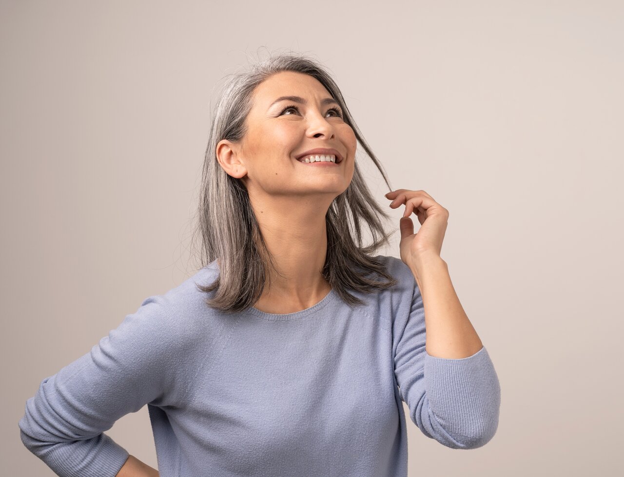 Portrait einer schönen Frau mit grauen Haaren und blau-grauem Pullover, die glücklich mit einer Haarsträhne spielt