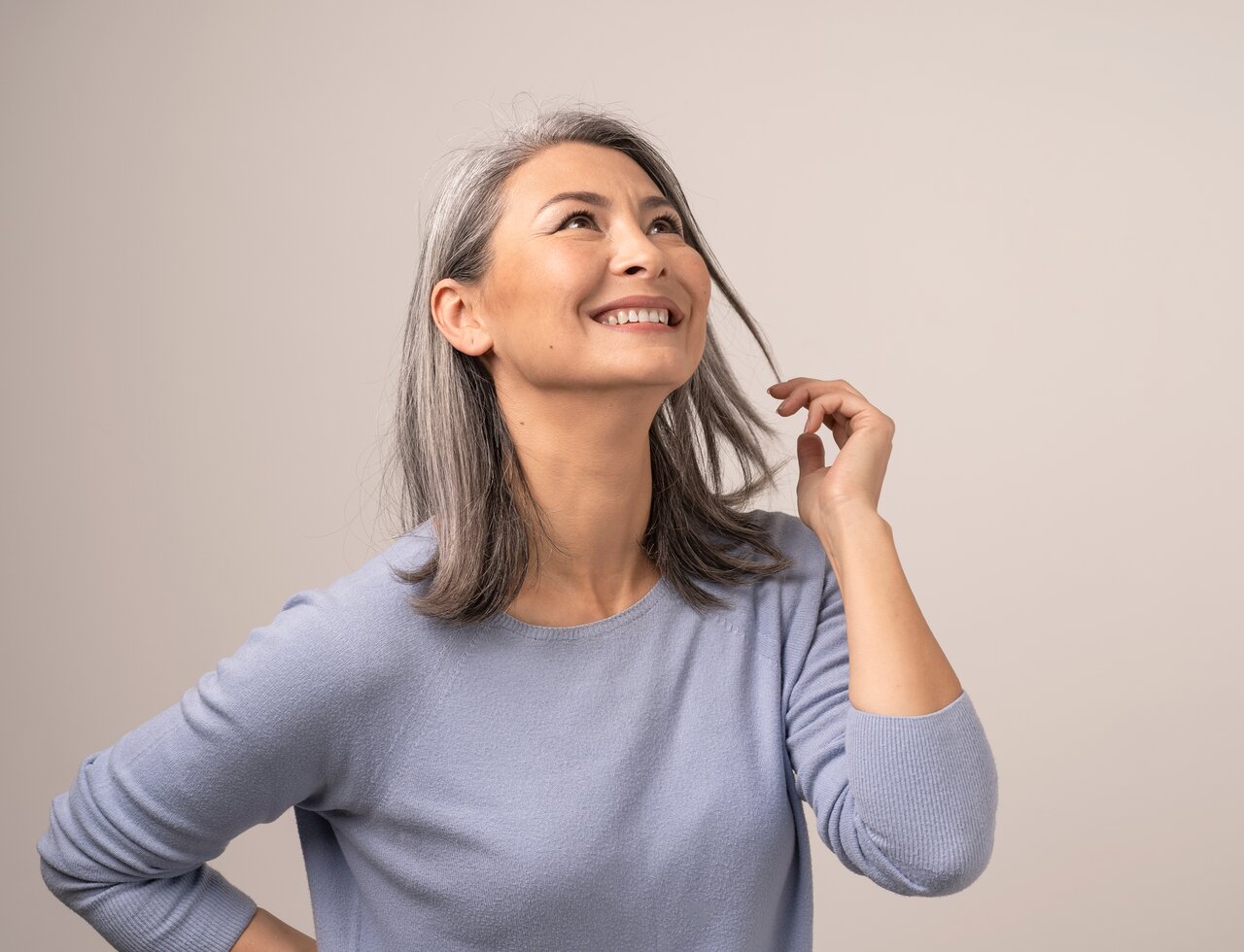 Bei grauem Haar verändert sich nicht nur die Haarfarbe, sondern auch die Haarstruktur Portrait einer schönen Frau mit grauen Haaren und blau-grauem Pullover, die glücklich mit einer Haarsträhne spielt