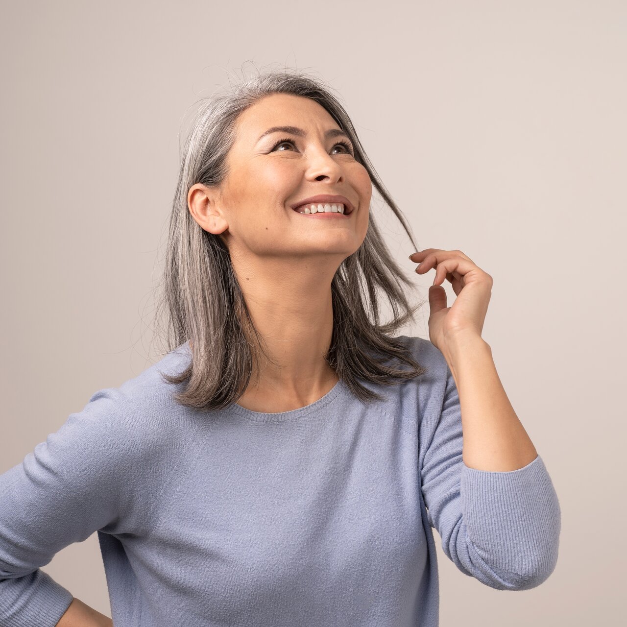 Portrait einer schönen Frau mit grauen Haaren und blau-grauem Pullover, die glücklich mit einer Haarsträhne spielt