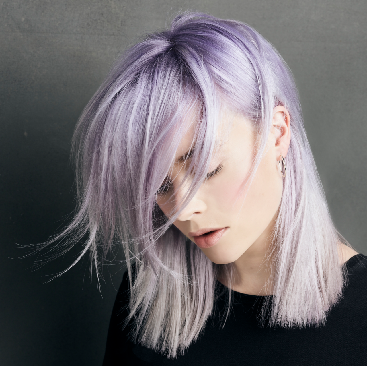 Farbshampoos pflegen, frischen die Haarfarbe auf und verleihen ausgefallene Farbnuancen – zum Beispiel Violett Portrait einer seitlich nach unten schauenden Frau, deren blonde Haare eine kühle Violett-Tönung zeigen