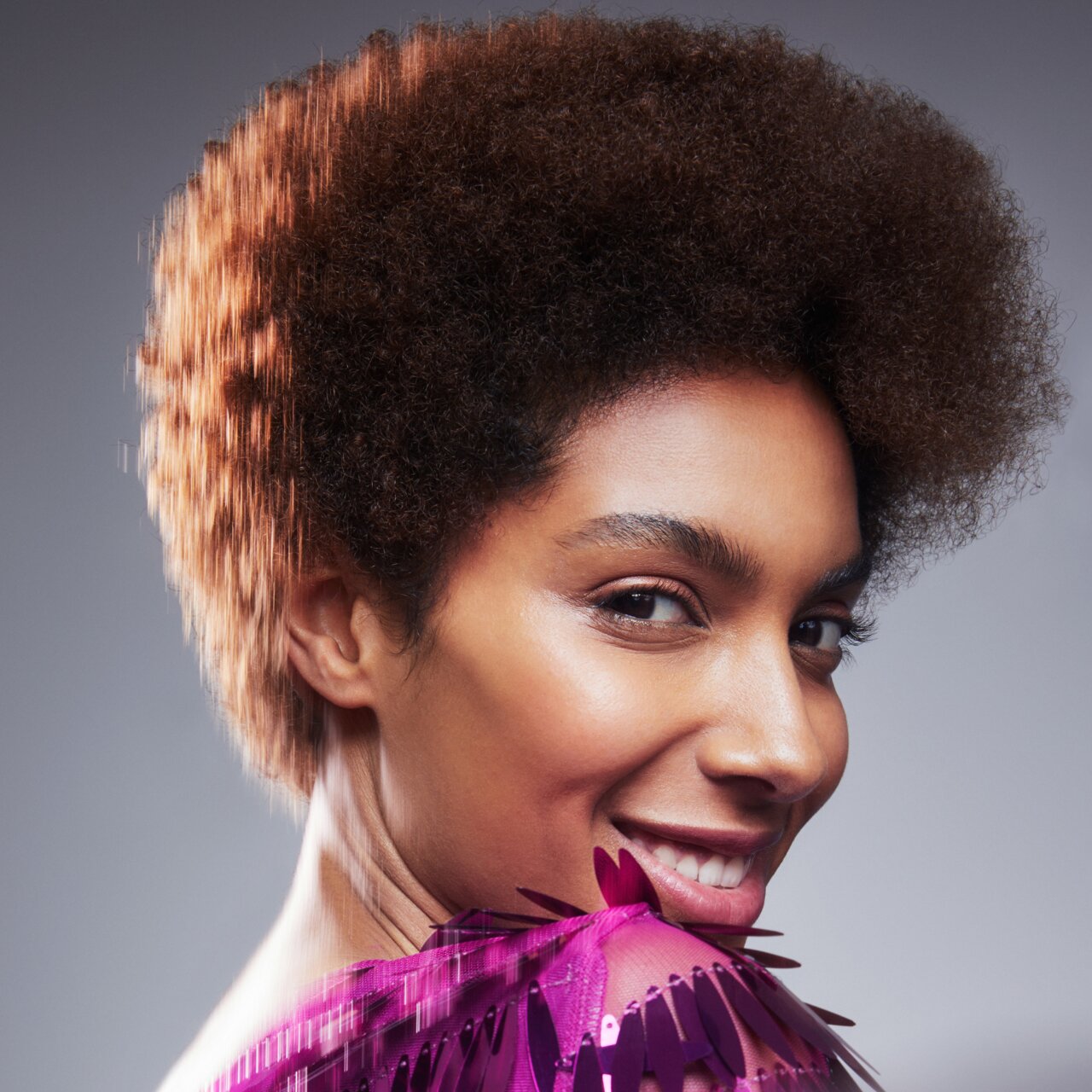 Porträt einer schönen jungen Frau mit Afro Frisur und heller gefärbten Spitzen als Sinnbild für den Haarfarben-Trend 2024 Sunkissed Curls