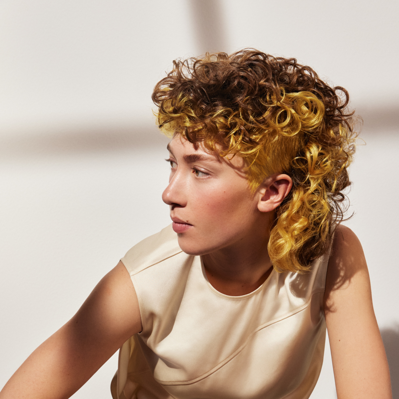 Porträt einer schönen jungen Frau mit einem Curly Mullet in der Trendhaarfarbe „Lemon Square“