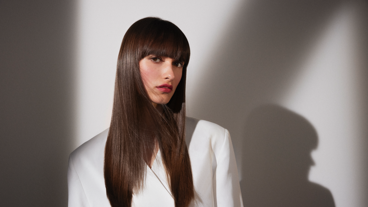 Schöne, junge Frau, deren dunkelbraune, lange Haare glatt und glänzend offen über Ihre Schulter fallen. 