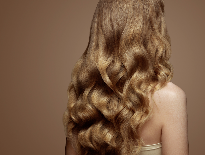 Rückenansicht einer Frau mit schönem langem, glänzendem welligem Haar als Sinnbild für die richtige Haarpflege bei trockenen Haaren im Winter