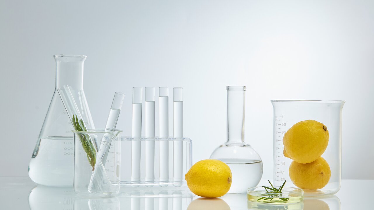 Reagenzgläser, Kolben und Messbecher, die mit klarer Flüssigkeit und Zitronen gefüllt sind als Sinnbild für den Einsatz von Vitamin C in der Hautpflege