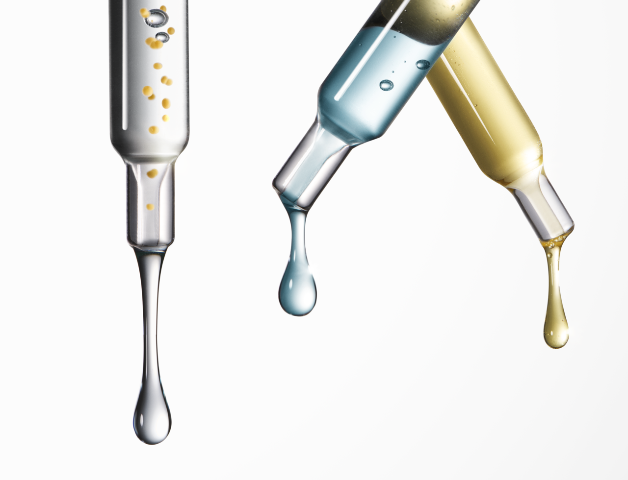 Nahaufnahme von drei Pipetten mit unterschiedlichen Flüssigkeiten gefüllt, aus deren unterer Öffnung der Inhalt tropft.