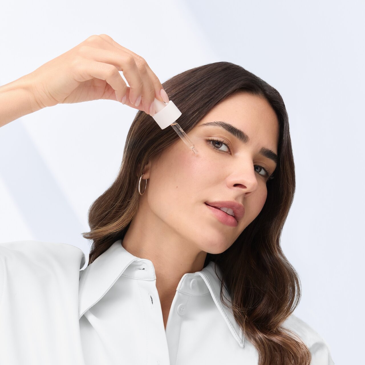 Schöne Frau mit einem frischen Teint hält eine Pipette gefüllt mit Coffein Booster an ihre Wange