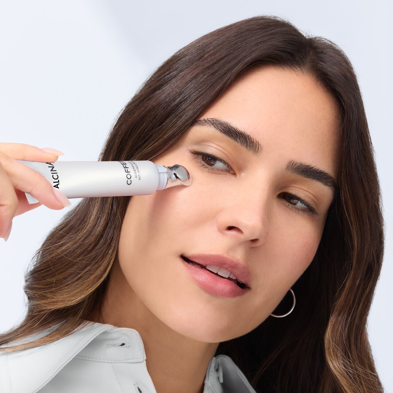 Schöne Frau trägt mit einem Applikator eine kühlende Augencreme unter ihren geschwollenen Augen auf