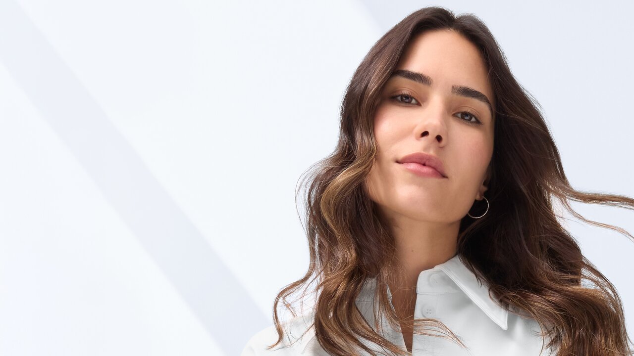 Schöne Frau mit rosigem Teint und langen braunen Haaren lächelt in die Kamera als Sinnbild für die Wirkung von Coffein-Hautpflege und Coffein für die Haare