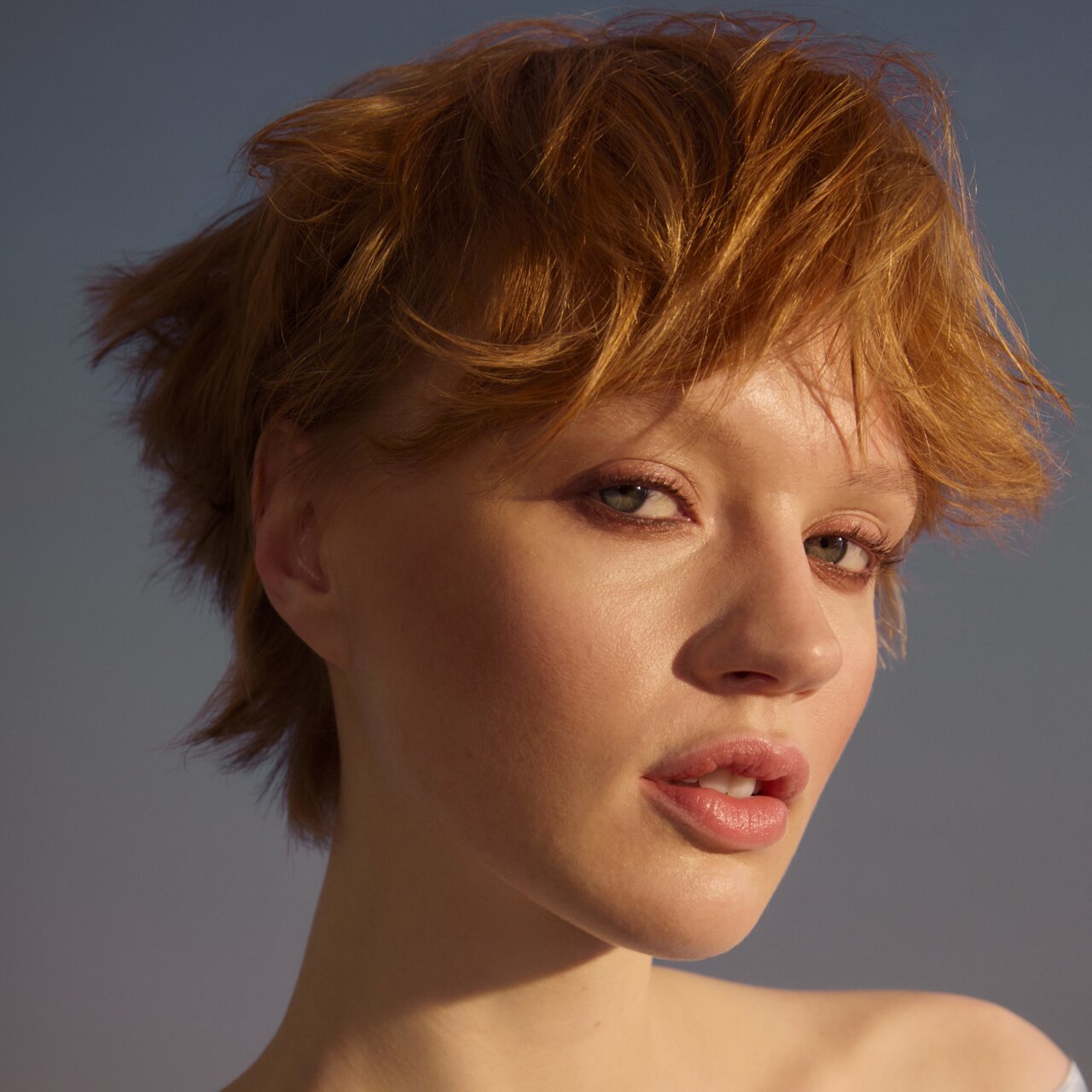 Junge Frau mit kurzen gestylten, rotblondem Haaren vor blauem Himmel