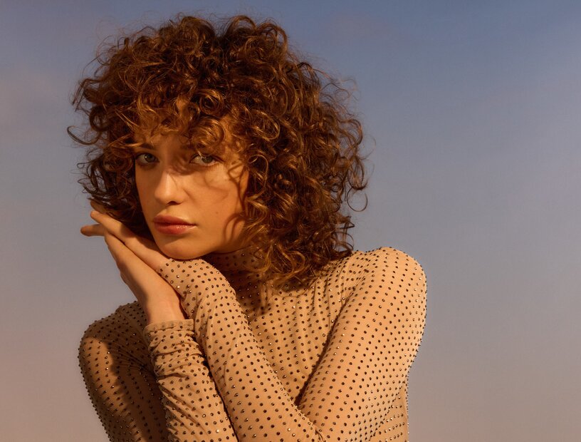 Portrait einer langhaarigen Frau mit zart gebräunter Haut, die aufmerksam in die Kamera schaut