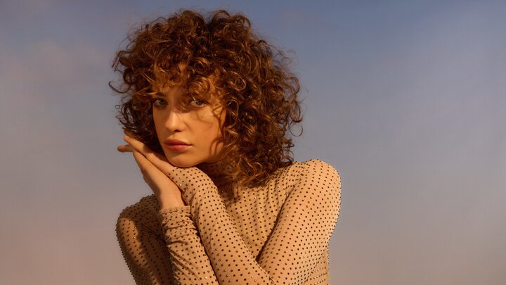 Portrait einer langhaarigen Frau mit zart gebräunter Haut, die aufmerksam in die Kamera schaut