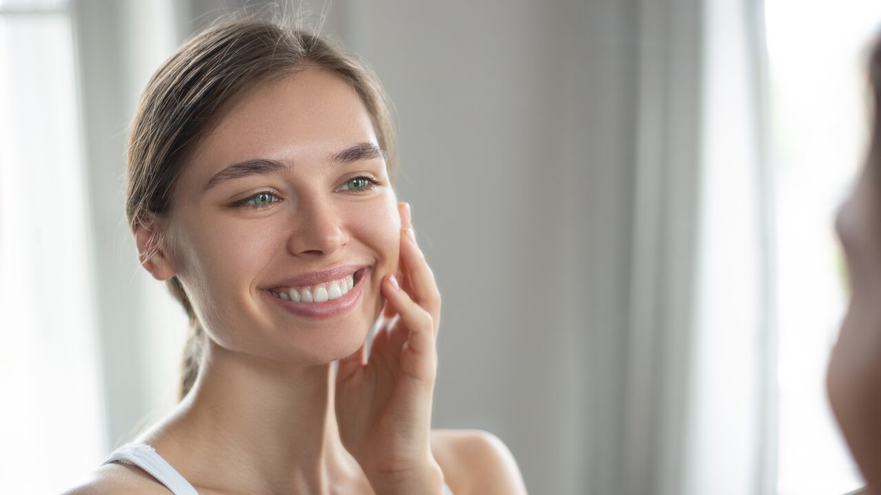 Portrait einer Frau, die sich selbst im Spiegel anlächelt und ins Gesicht fasst