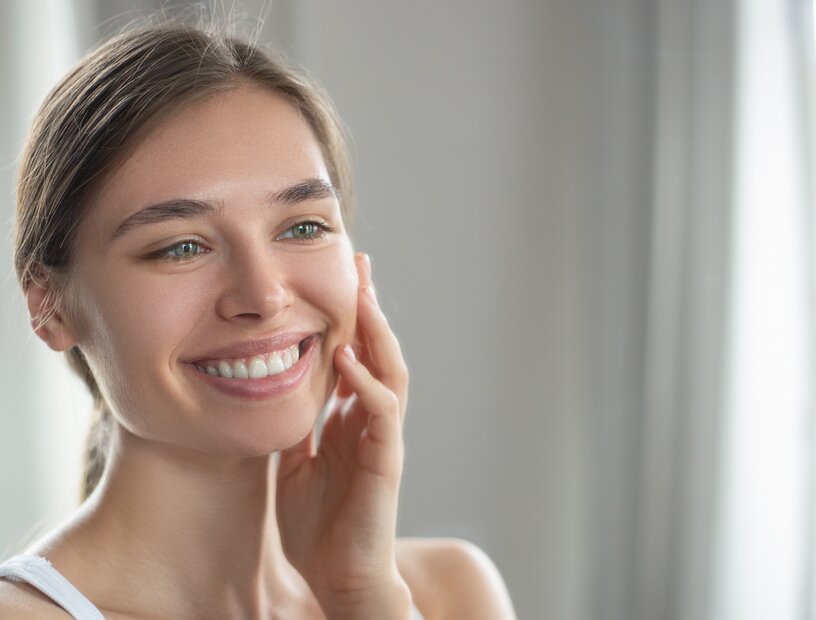 Portrait einer Frau, die sich selbst im Spiegel anlächelt und ins Gesicht fasst