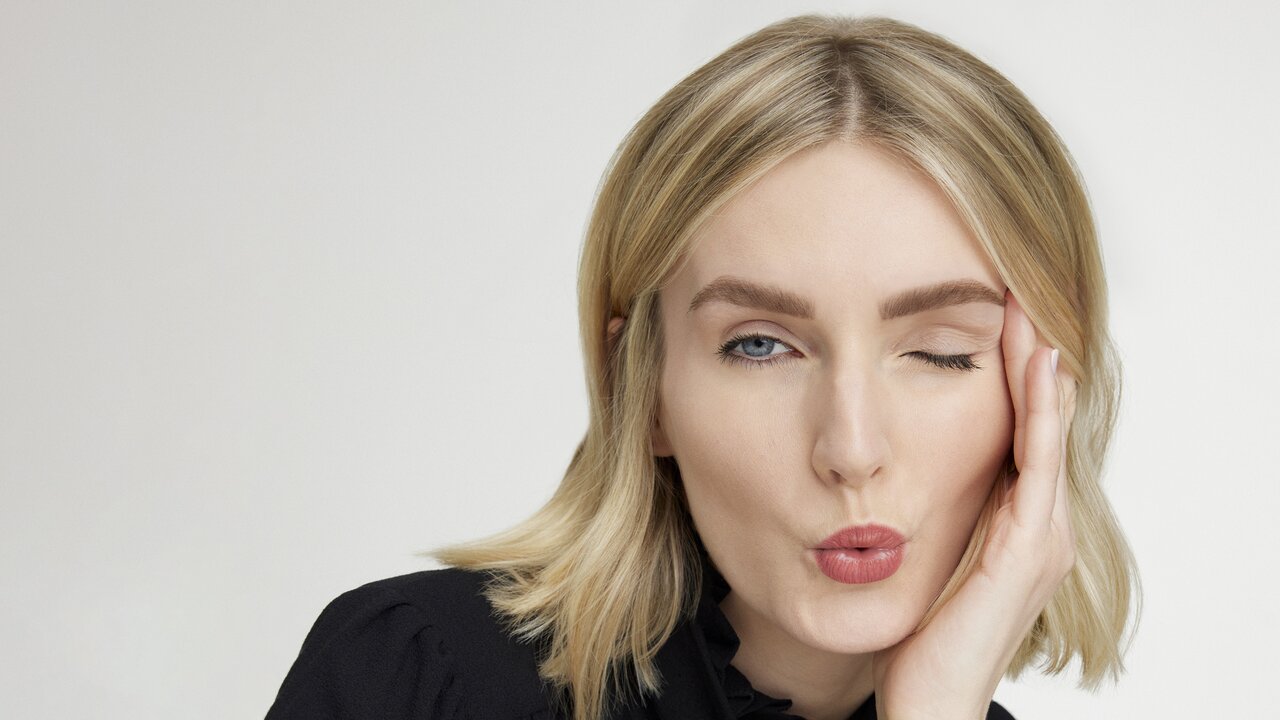 Portrait einer Frau mit ausdrucksstarken Augenbrauen, die keck mit Kussmund und einem Augenzwinkern in die Kamera blickt