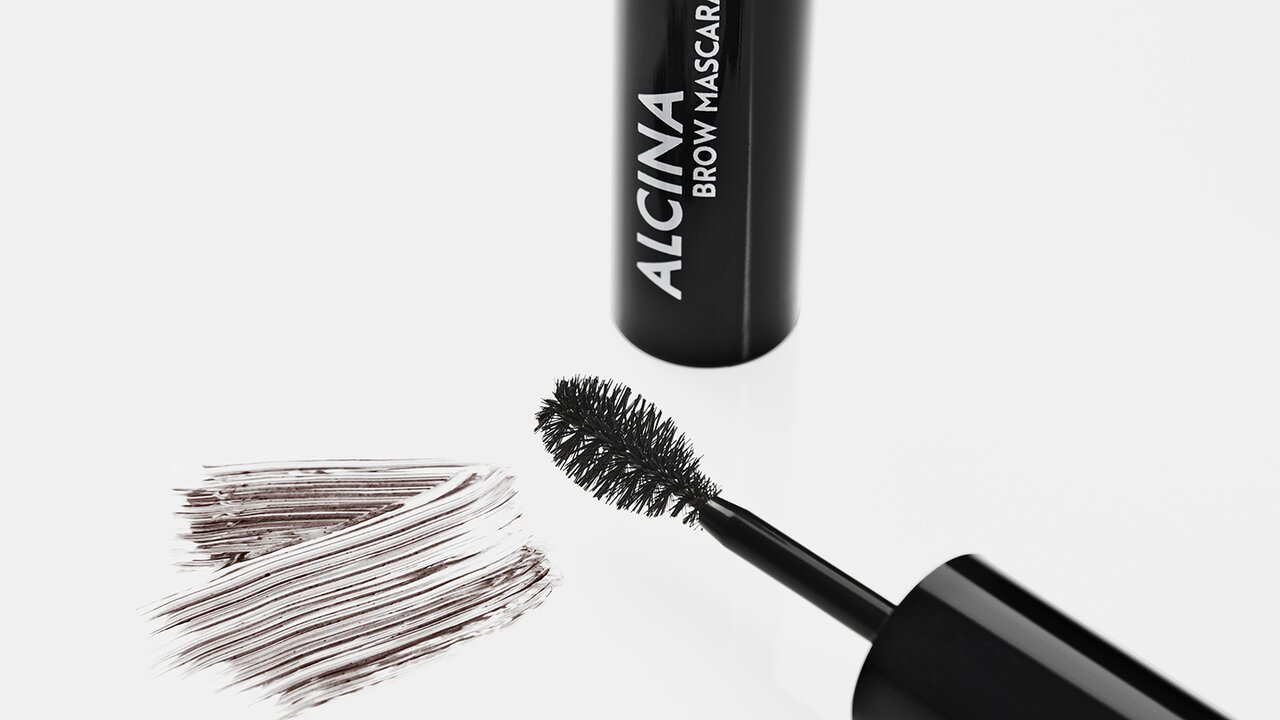 ALCINA Augenbrauen Mascara: Applicator, Behälter und feine braune Farbstriche auf hellem Grund