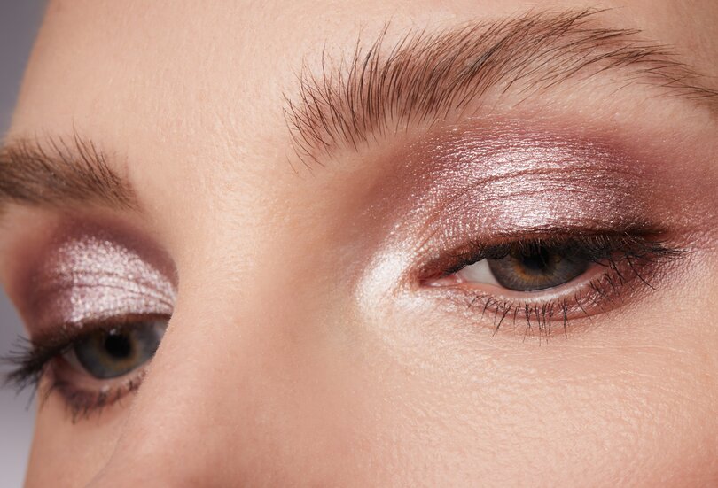 Nahaufnahme einer schönen jungen Frau mit stark geschminkten Augen mit rosa Lidschatten und Metallic Effekt als Sinnbild für den Make-up-Trend Metallic Glamour im Herbst Winter 2023
