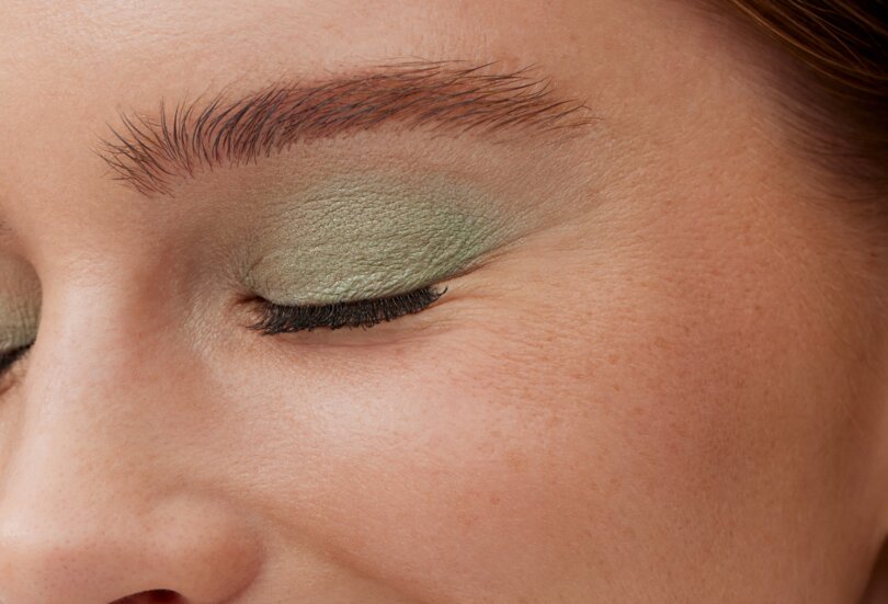Nahaufnahme einer schönen jungen Frau mit Glitzer Lidschatten in der Farbe Mintgrün als Sinnbild für den Make-up Trend Shimmering Eyes im Frühling Sommer 2024